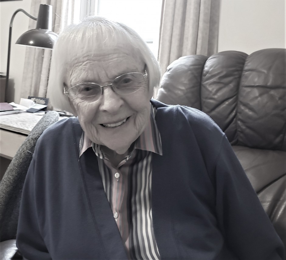 Elderly woman wearing blue cardigan and glasses smiling
